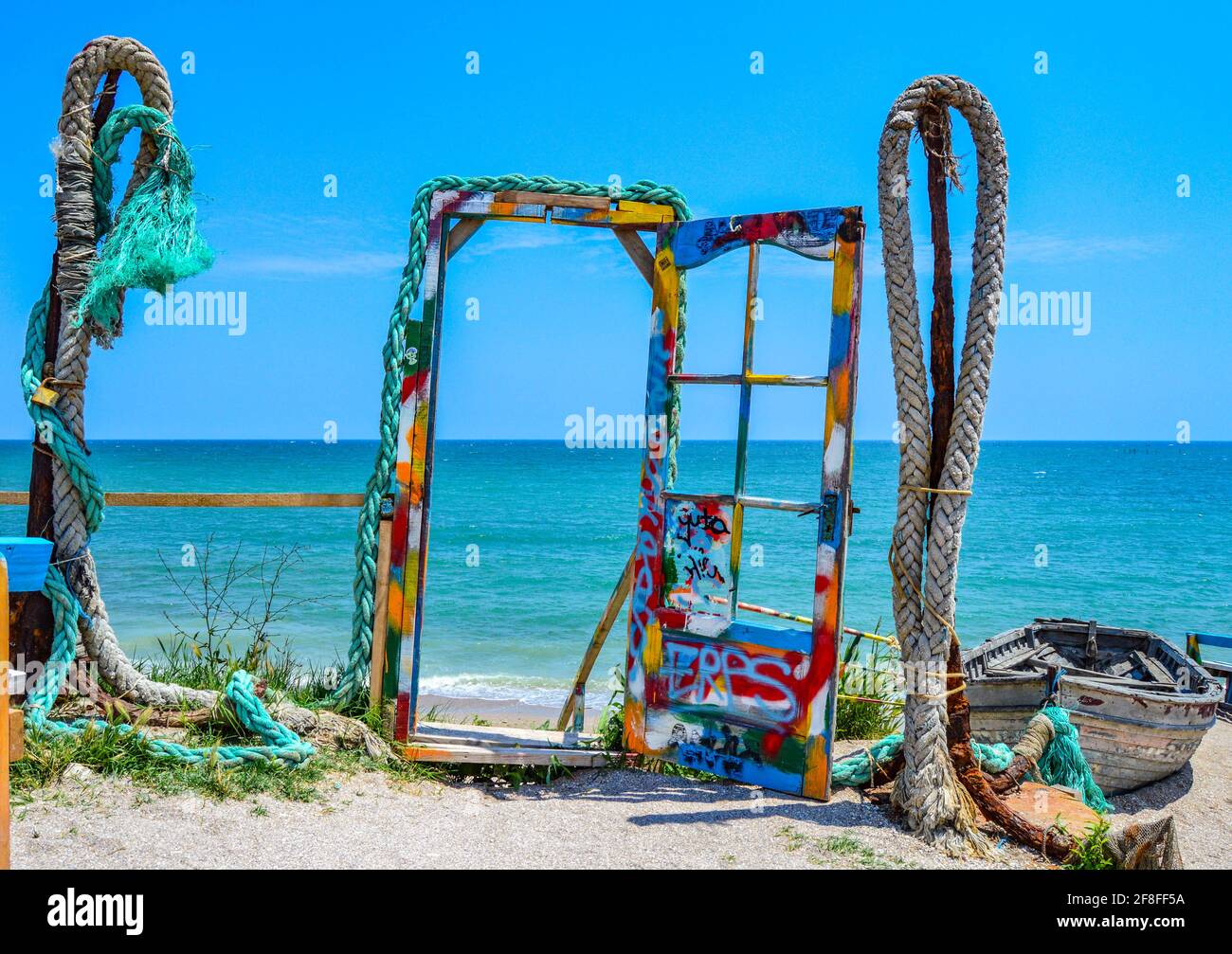 Landschaftsfoto von farbenfrohen Installationen am Strand, farbigen Seilen und einer Tür, die an einem sonnigen Sommertag mit blauem Himmel zum Schwarzen Meer führt Stockfoto