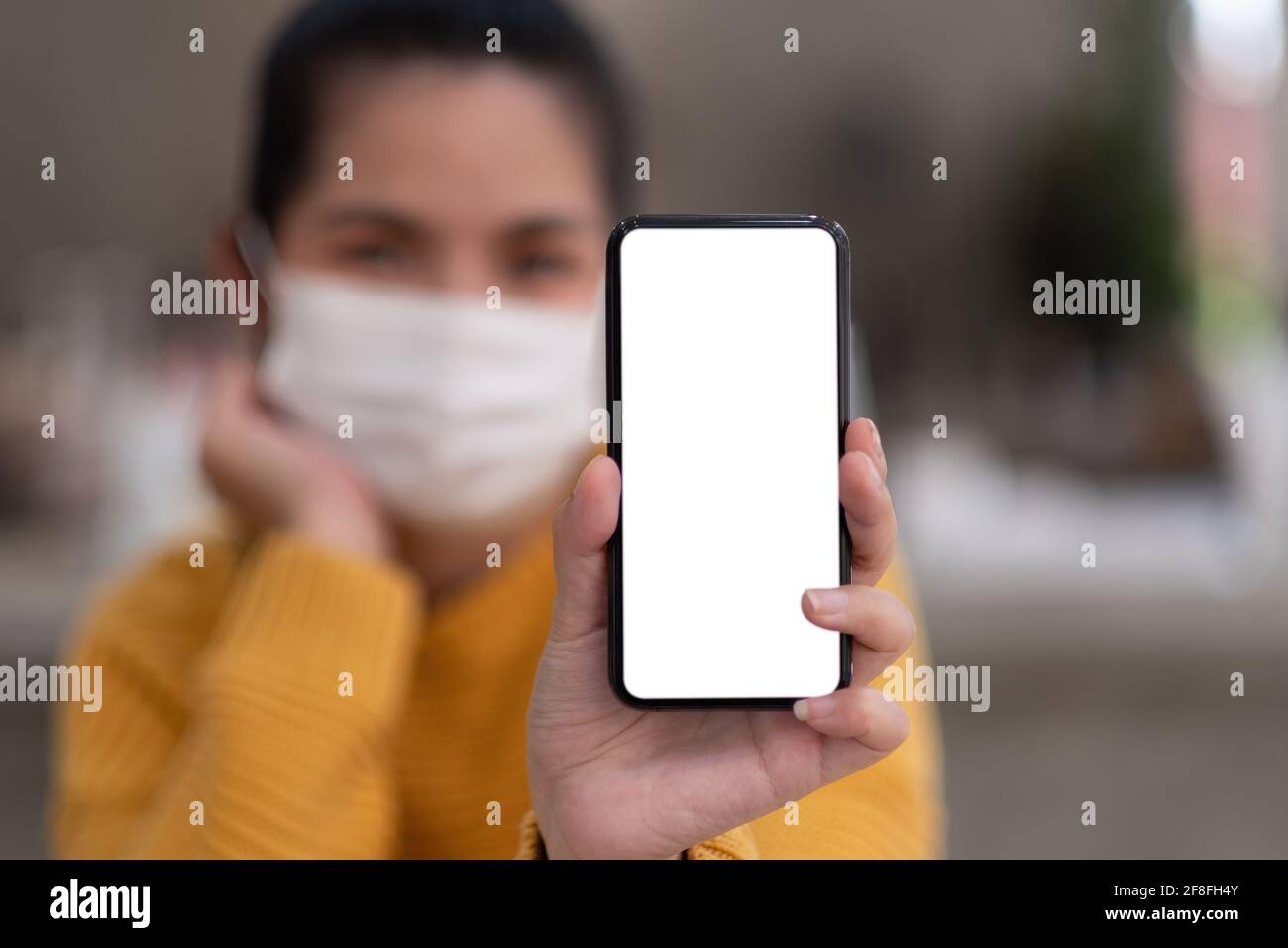 Mockup-Bild einer schönen Frau tragen Maske, während das Mobiltelefon mit leerem weißen Bildschirm halten. Stockfoto