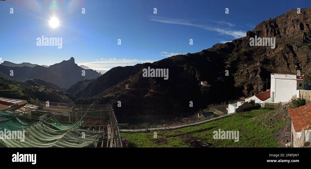 Panoramablick auf ein rustikales Land mit Gebäuden und ein Felsiger Berg vor dem Hintergrund der strahlenden Sonne Stockfoto