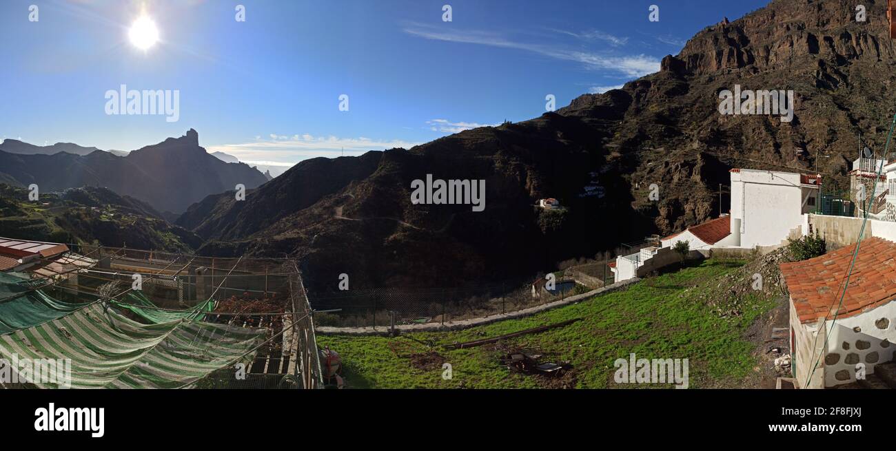 Panoramablick auf ein rustikales Land mit Gebäuden und ein Felsiger Berg vor dem Hintergrund der strahlenden Sonne Stockfoto