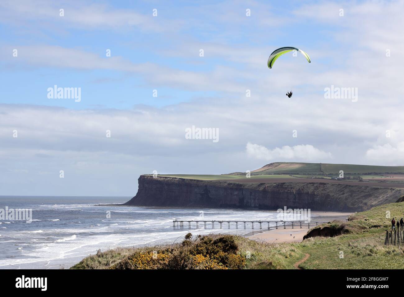 Gleitschirm Fliegen Sie entlang der Küste mit dem Saltburn Pier und den Klippen von Huntcliff unten, Saltburn-by-the-Sea mit dem North Yorkshire, Großbritannien Stockfoto