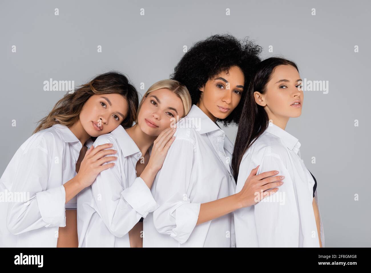 Multiethnische Frauen in weißen Hemden, die sich gleichzeitig anlehnen Blick auf die Kamera isoliert auf Grau Stockfoto