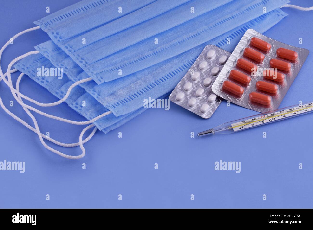 Schützende medizinische Maske, Pillen, Thermometer auf blauem Hintergrund, Corona-Virus-Schutz, Coronavirus, covid19 Globale Pandemie Stockfoto