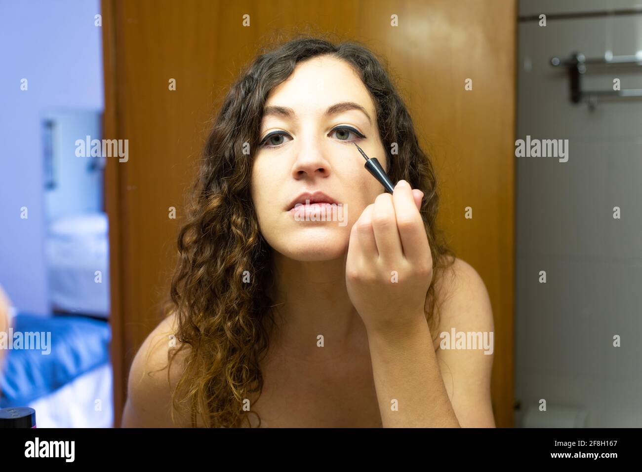 Junge Frau, die sich vor einem Spiegel schminkt. Nahaufnahme mit Augenlinse, Zeichnung der Augenlinie. Stockfoto