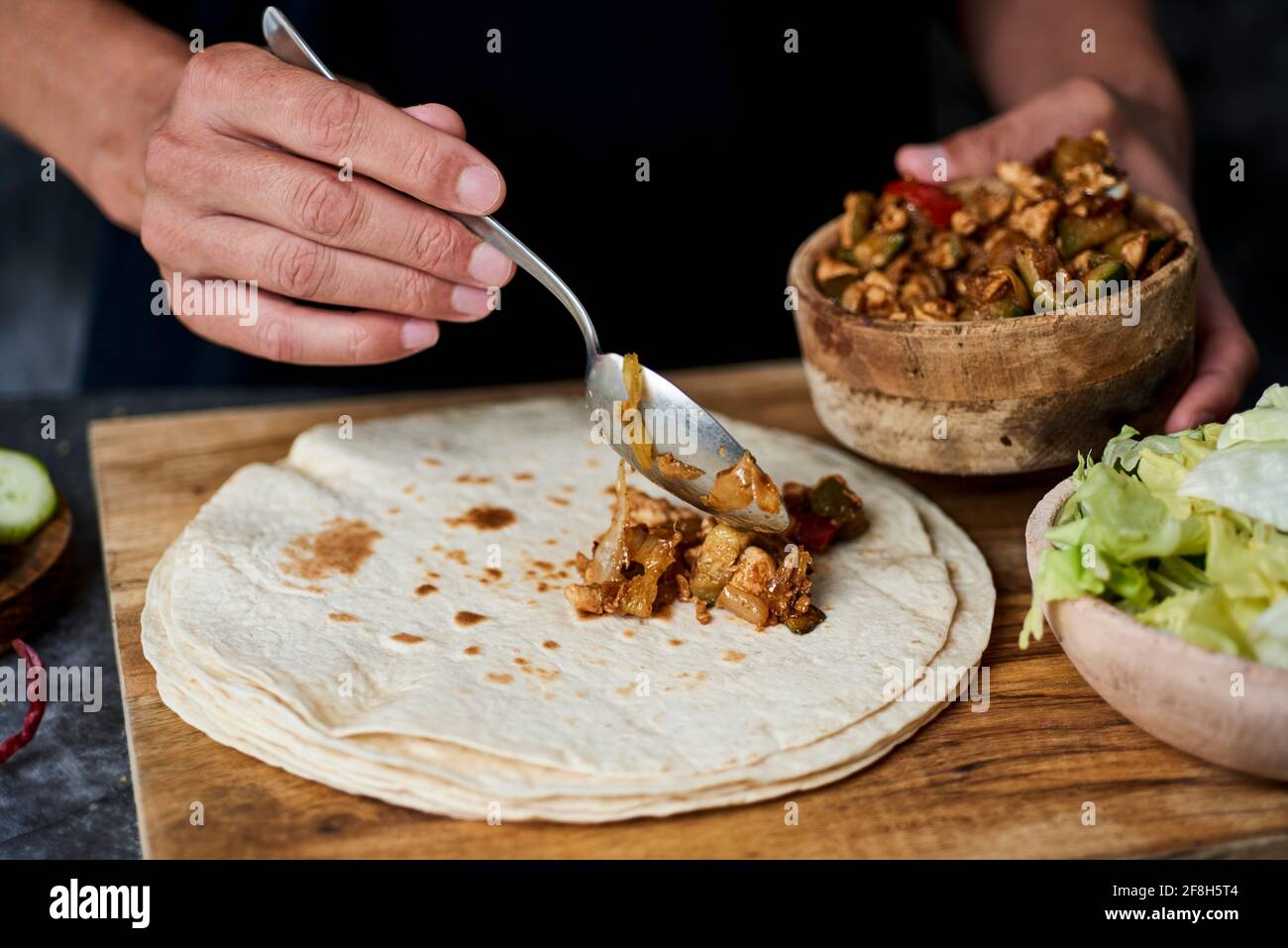 Ein junger Kaukasier füllt ein Durum oder einen Burrito mit Hühnerfleisch, das mit verschiedenen Gemüsesorten wie Zwiebeln oder rotem und grünem Pfeffer zubereitet wird Stockfoto