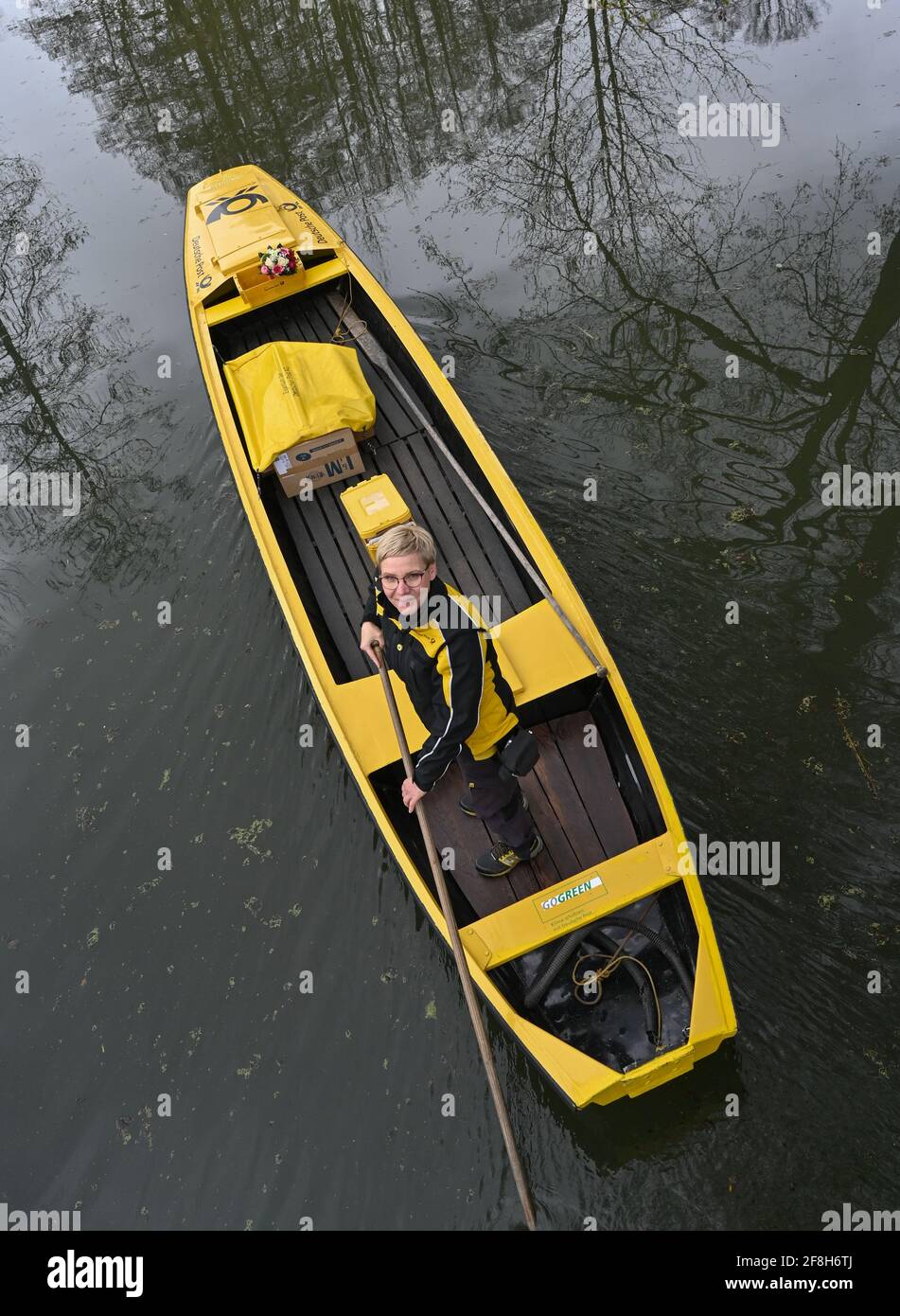 Brandenburg, Lehde: 14. April 2021, Andrea Bunar, Postzustellerin, ist mit ihrem gelben Briefkahn zu Beginn der Postzustellsaison auf einem Fluss (Wasserweg im Spreewald). Die Postträgerin Andrea Bunar bringt in der Corona-Pandemie ein wenig Normalität in den Spreewald: Seit Mittwoch (14.04.2021) liefert sie wieder Briefe und Pakete an Bewohner auf ihrem Lastkahn. Die 50-Jährige liefert an 65 Haushalte, sie steuert ihren Lastkahn auf der rund acht Kilometer langen Tour allein mit Muskelkraft. (Zu dpa: 'Briefträger mit Muskelkraft: Post kommt wieder im Spreewald b Stockfoto