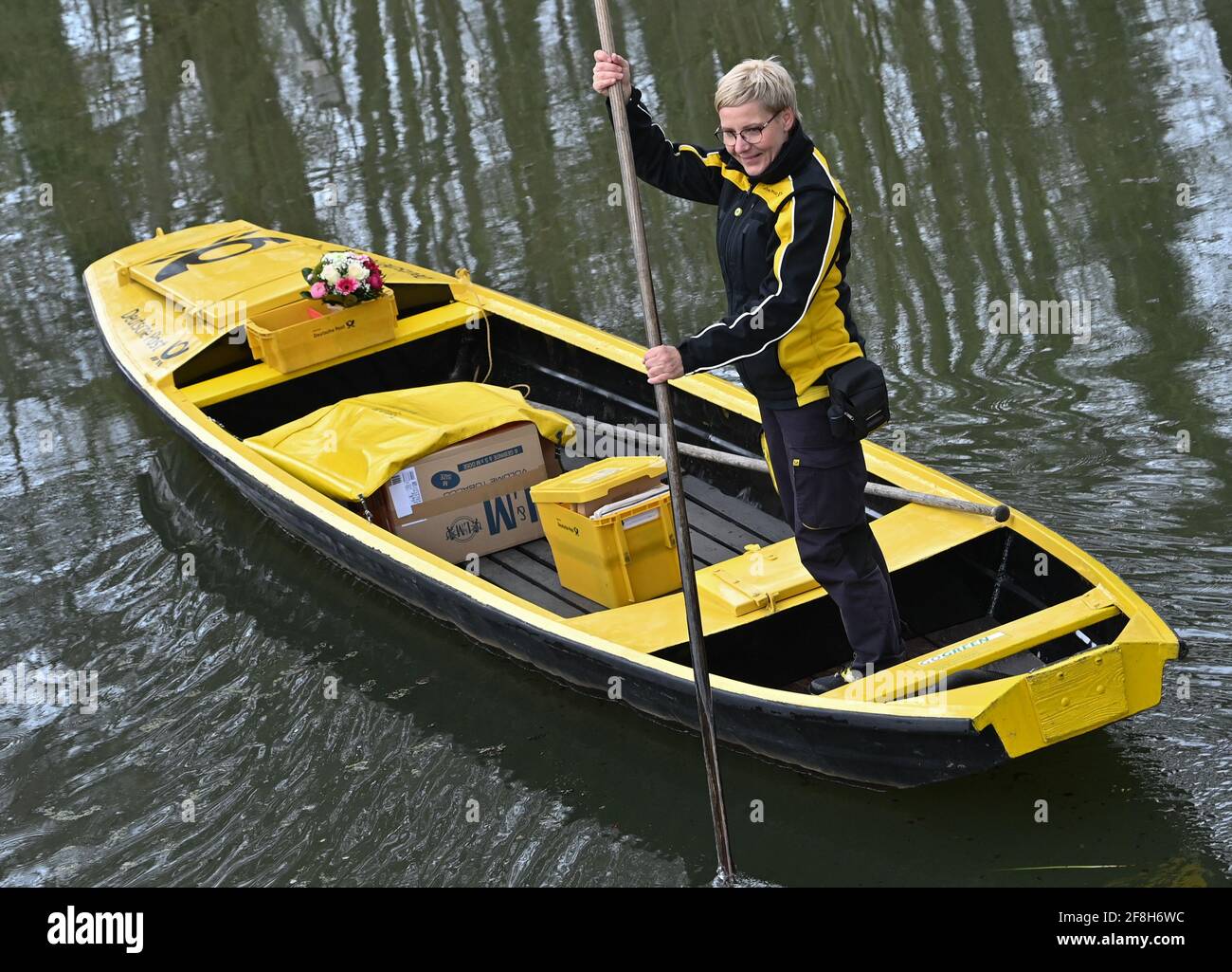 Brandenburg, Lübbenau 14. April 2021: Andrea Bunar, Postträgerin, fährt zu Beginn der Versandsaison ihren gelben Briefkahn über einen Fluss (Wasserstraße im Spreewald). Die Postträgerin Andrea Bunar bringt während der Corona-Pandemie ein wenig Normalität in den Spreewald: Seit Mittwoch (14.04.2021) liefert sie mit ihrem Lastkahn wieder Briefe und Pakete an die Bewohner. Die 50-Jährige liefert an 65 Haushalte, sie steuert ihren Lastkahn auf der rund acht Kilometer langen Tour allein mit Muskelkraft. (An dpa: 'Briefträger mit Muskelkraft: Post kommt in die Spreewald ag. Stockfoto