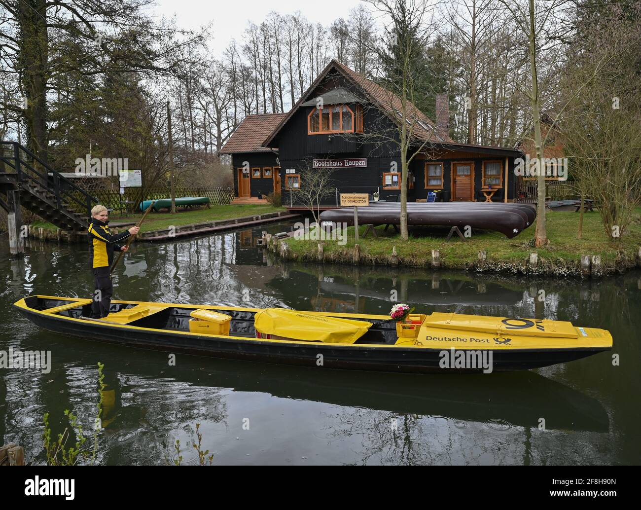 14. April 2021, Brandenburg, Lübbenau: Andrea Bunar, Postträgerin, fährt zu Beginn der Versandsaison ihren gelben Briefkahn über einen Fluss (Wasserweg im Spreewald). Die Postträgerin Andrea Bunar bringt während der Corona-Pandemie ein wenig Normalität in den Spreewald: Seit Mittwoch (14.04.2021) liefert sie mit ihrem Lastkahn wieder Briefe und Pakete an die Bewohner. Die 50-Jährige liefert an 65 Haushalte, sie steuert ihren Lastkahn auf der rund acht Kilometer langen Tour allein mit Muskelkraft. (An dpa: 'Briefträger mit Muskelkraft: Post kommt in die Spreewald ag. Stockfoto