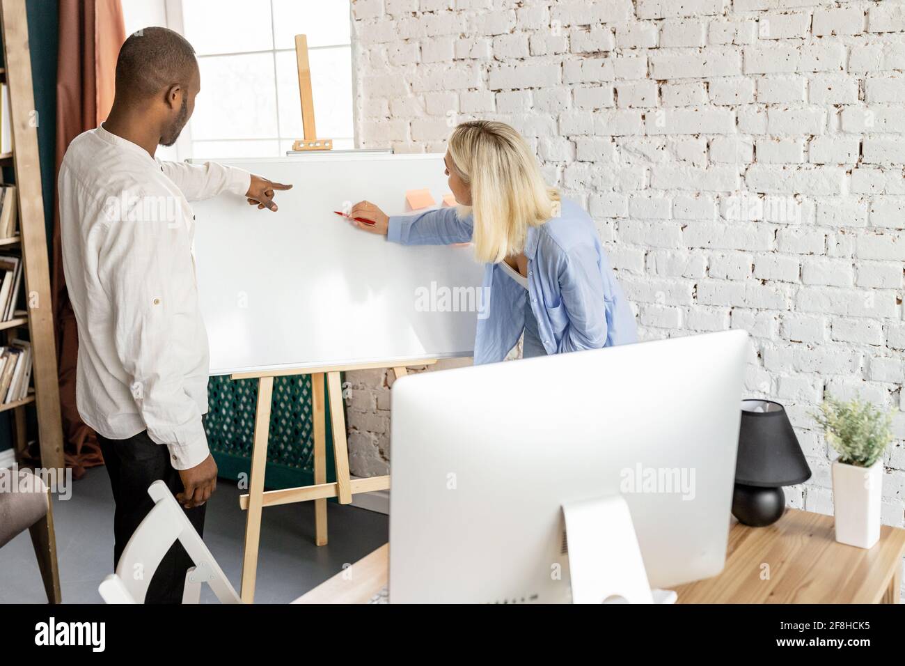 Seriöse, multirassische Kollegen arbeiten gemeinsam an einem Projekt im Büro und schreiben neue Ideen für das Startup auf dem Markerboard. Konzentriertes Geschäft Stockfoto