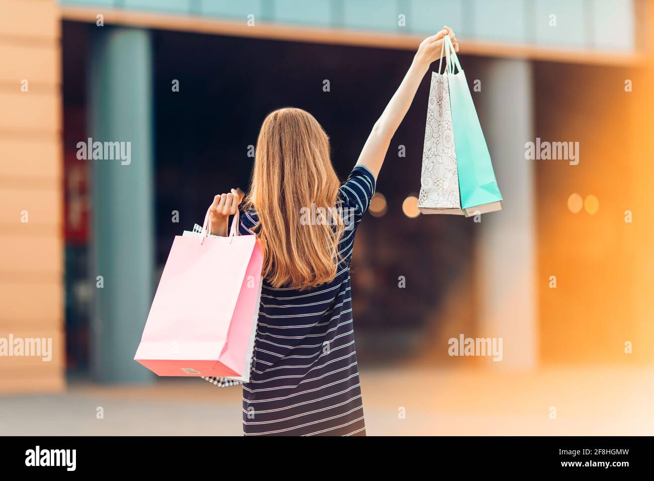 Rückansicht, eine glückliche, attraktive junge Frau in Sonnenbrillen, Shopping in der Mall, Einkaufstaschen in der Hand. Mode Stockfoto