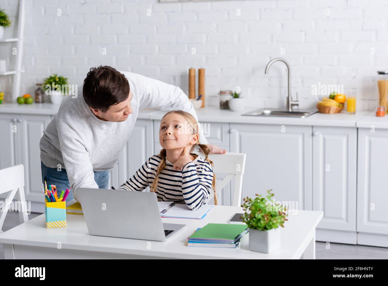 Vater und Tochter schauen sich während des Online-Unterrichts an In der Küche Stockfoto
