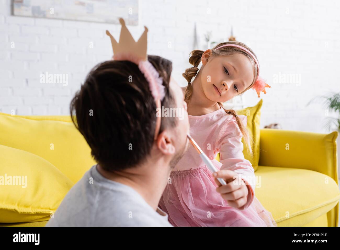 Kind in der Spielzeugkrone, das Vater auf verschwommen ins Gesicht stielt Vordergrund Stockfoto