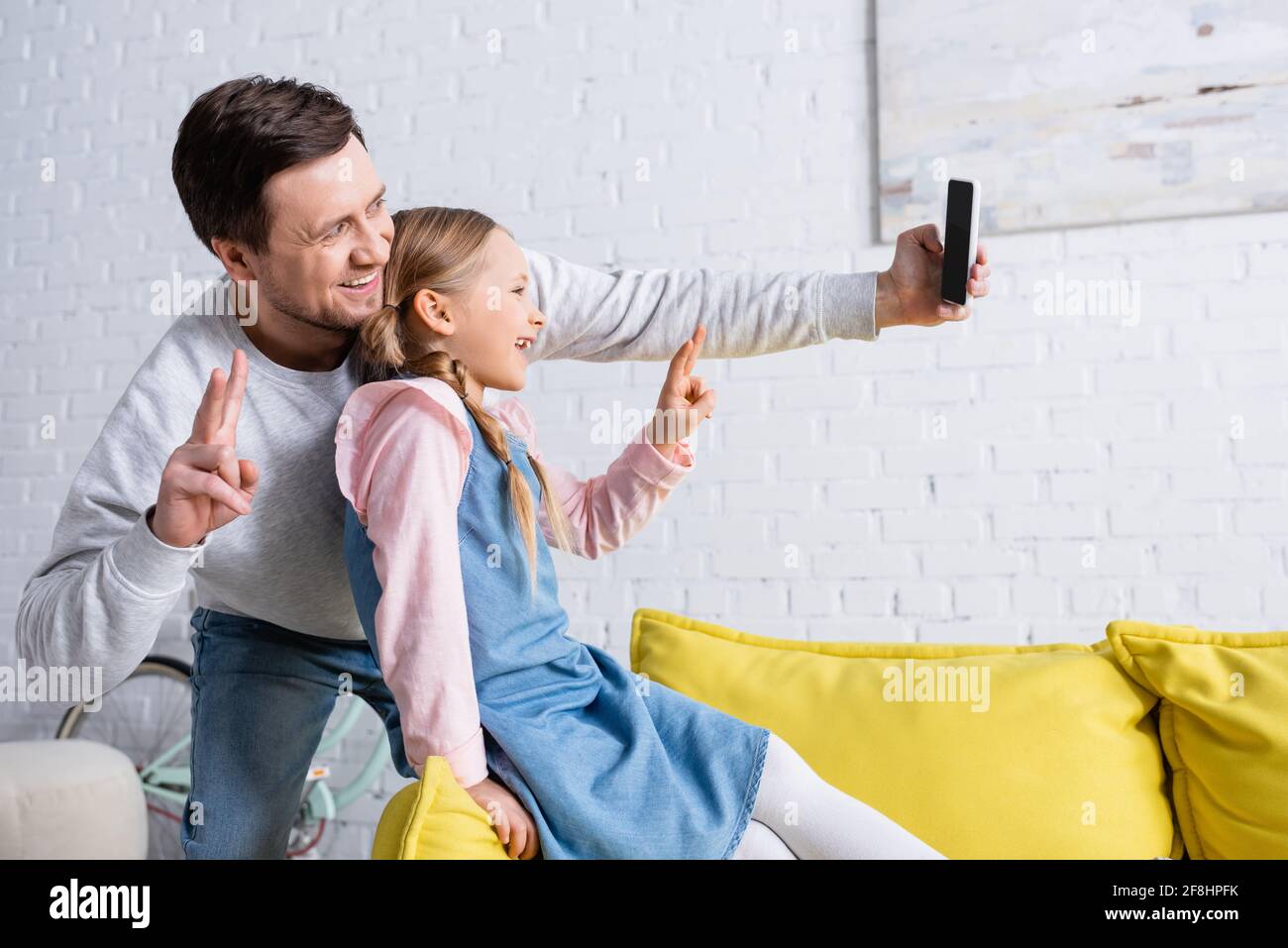 Fröhlicher Vater und Tochter zeigen beim Selfie eine Siegesgeste Auf dem Smartphone Stockfoto