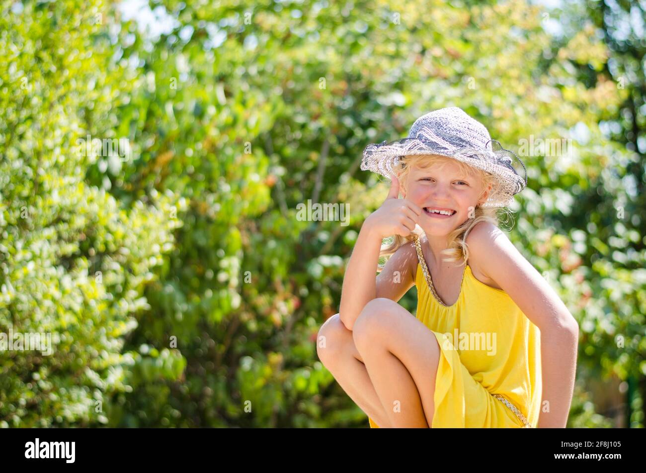 Kleine blonde Mädchen in gelbem Kleid zeigt ja Geste Stockfoto