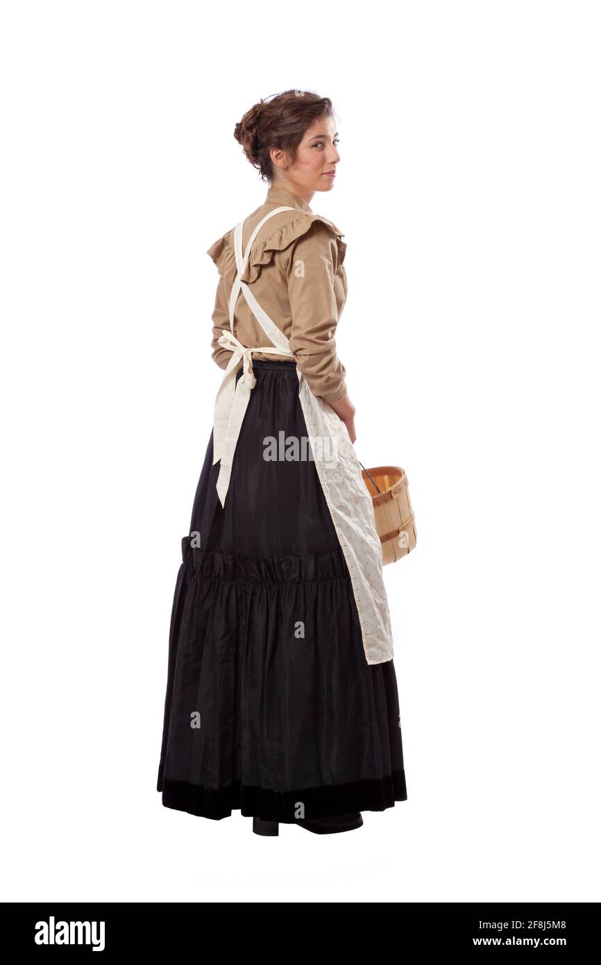 Junge Präriefrau mit Schürze, die zurückschaut und einen hält Korb isoliert auf weiß Stockfoto