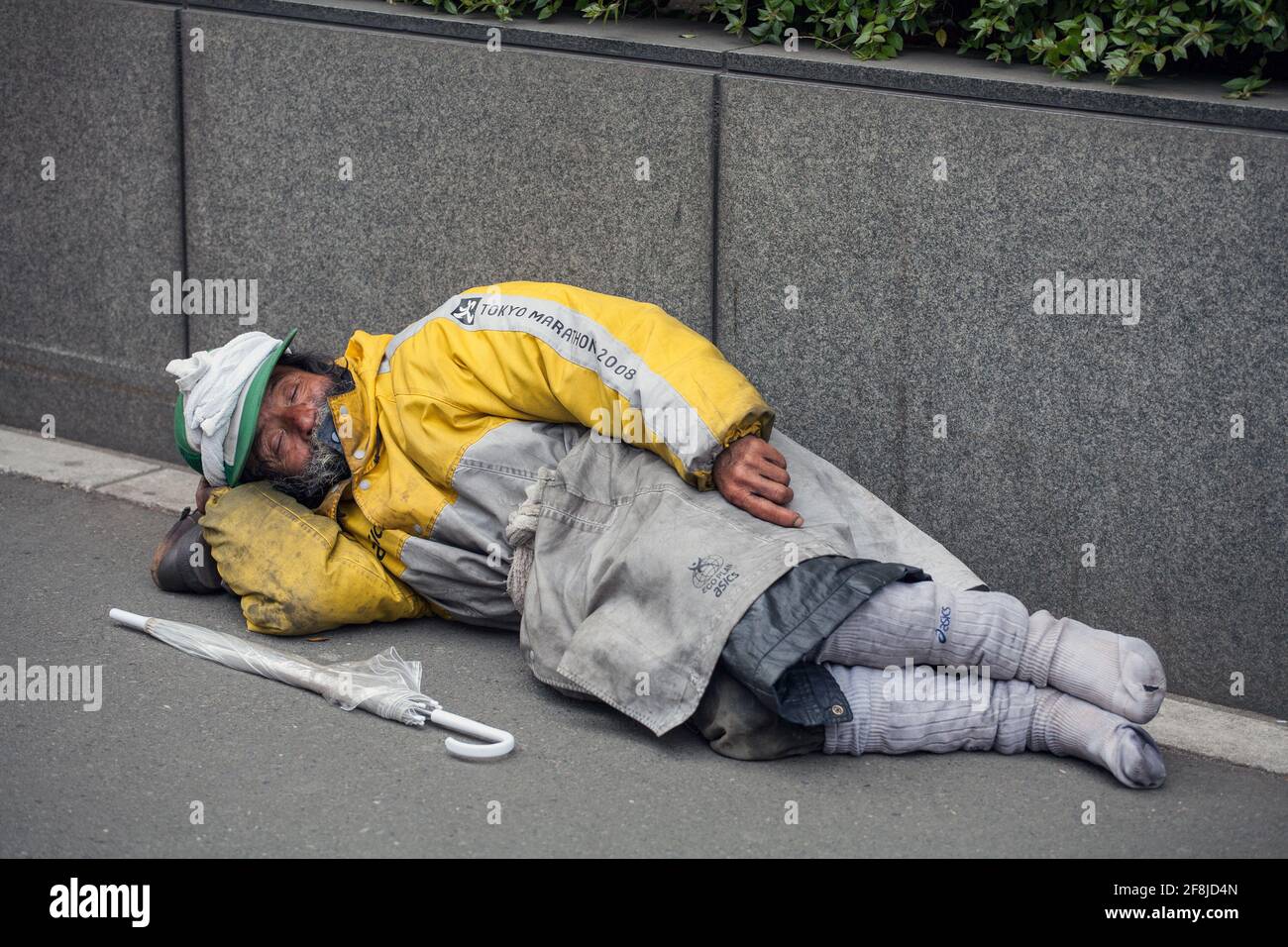 Obdachlose japanische Männer legten sich auf der Straße neben einem Regenschirm nieder, Aoyama, Tokio, Japan Stockfoto