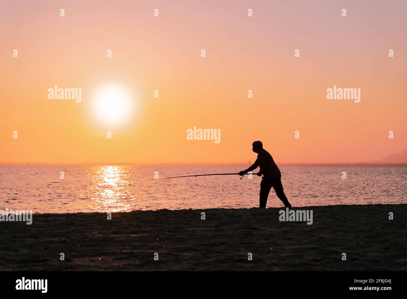 Silhouette der Mann Angeln in Wellen am Strand bei Sonnenuntergang Stockfoto