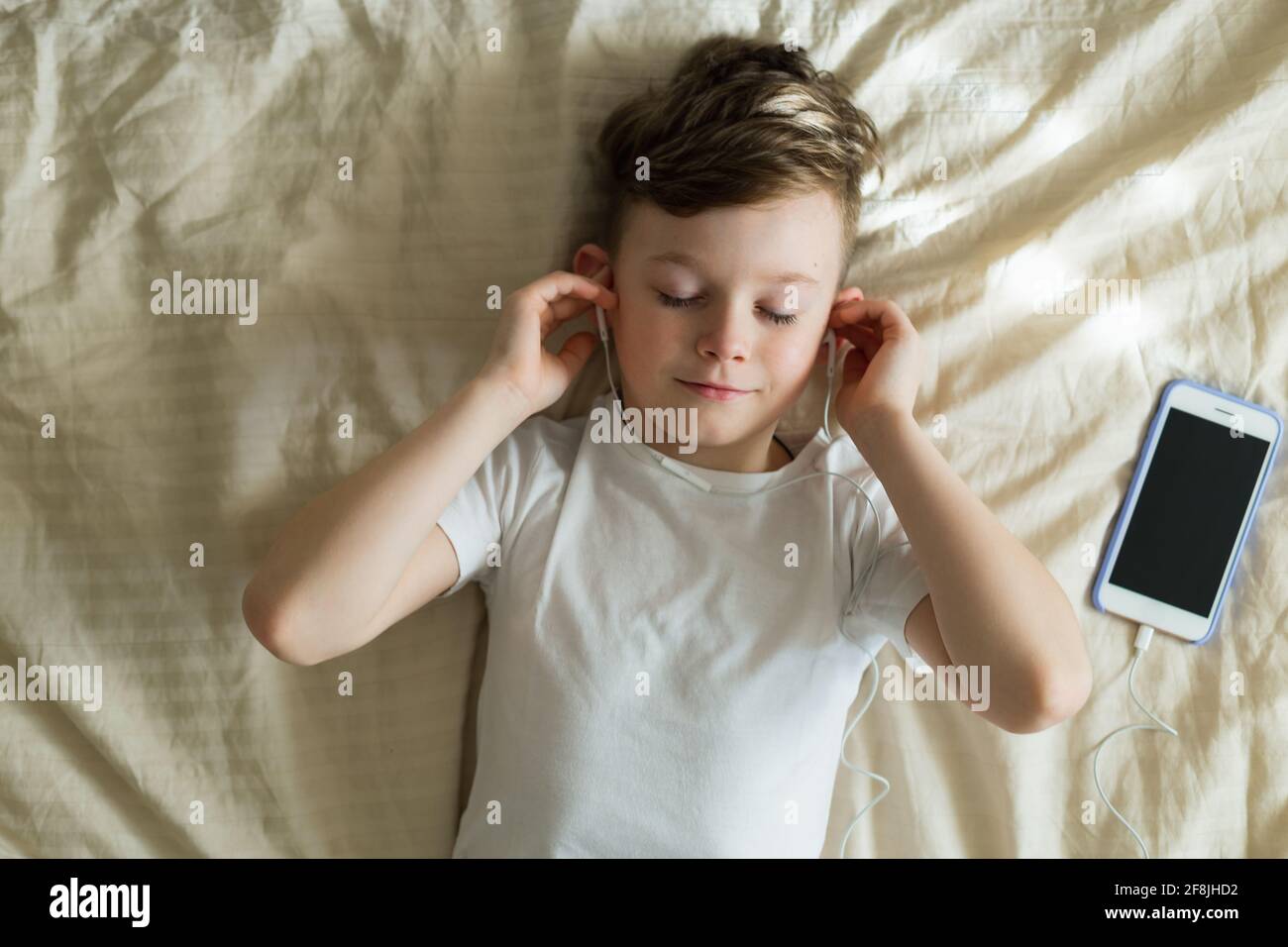 Junge hört Musik mit Kopfhörern auf dem Bett Stockfoto