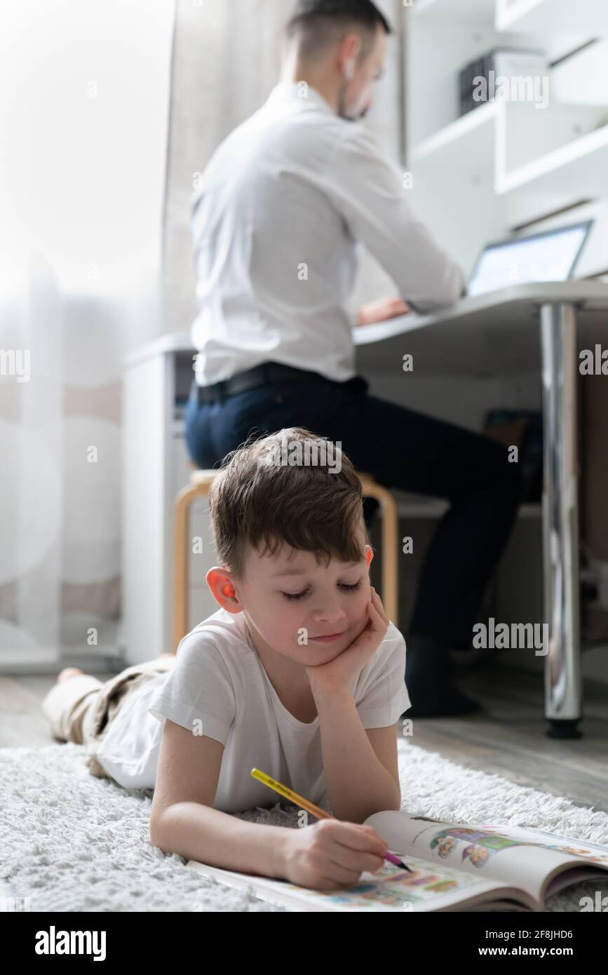 Junge macht Hausaufgaben in der Nähe des Vaters arbeiten Stockfoto