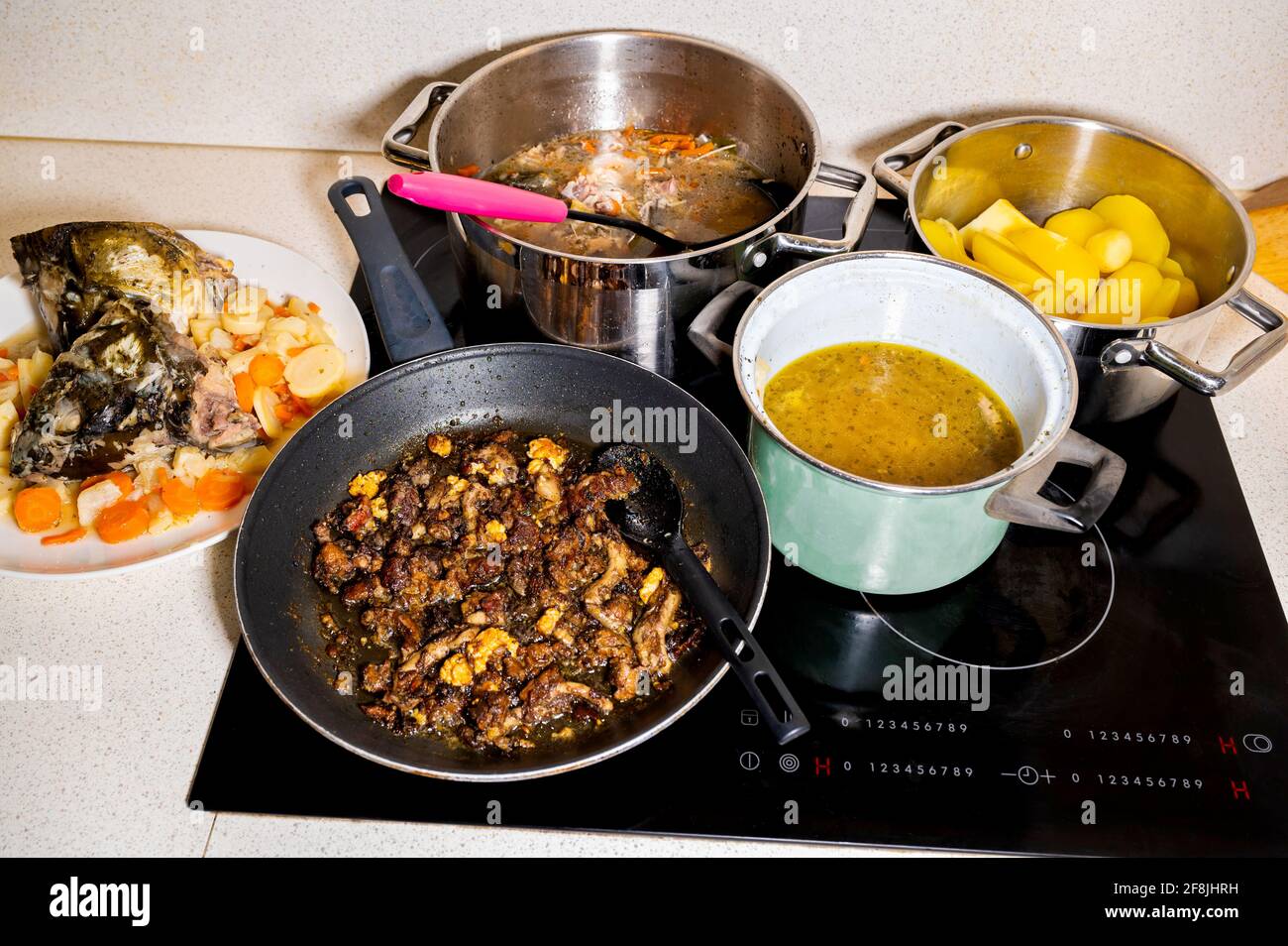 Zubereitung der Mahlzeit in vielen Töpfen auf Keramikherd in der Küche. Kochende Fischsuppe mit Gemüse, Kartoffeln, Karpfenkopf, Körper und Innereien. Stockfoto