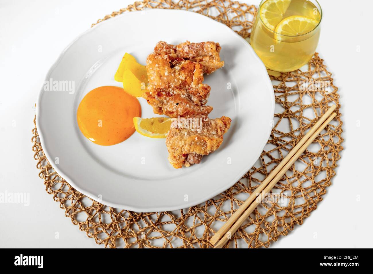 Gebratene panierte Hähnchenstücke mit eingelegtem Daikon und Mayonnaise, Essstäbchen und hausgemachtem Eistee auf Bambusmatte auf weißem Hintergrund, Nahaufnahme. Stockfoto