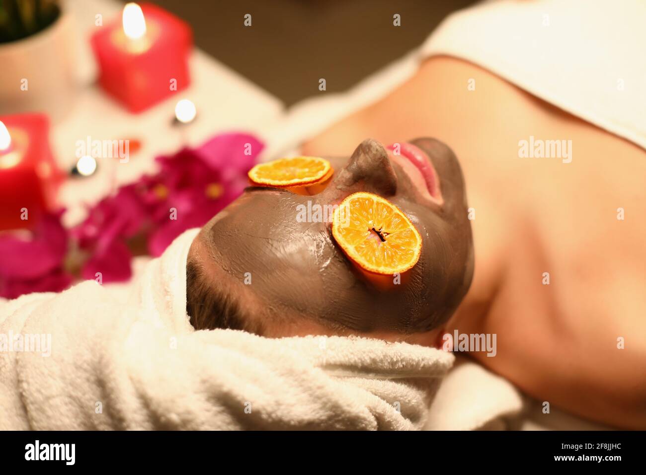 Frau, die im Spa-Salon mit einer Tonmaske auf ihr liegt Gesicht und orangefarbene Scheiben auf den Augen Stockfoto