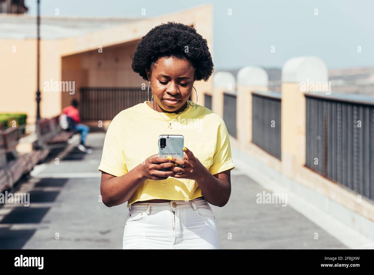 Porträt eines schwarzen Mädchens mit afrohaaren und Reifringen, das ihr Handy benutzt und in einem städtischen Raum läuft. Stockfoto
