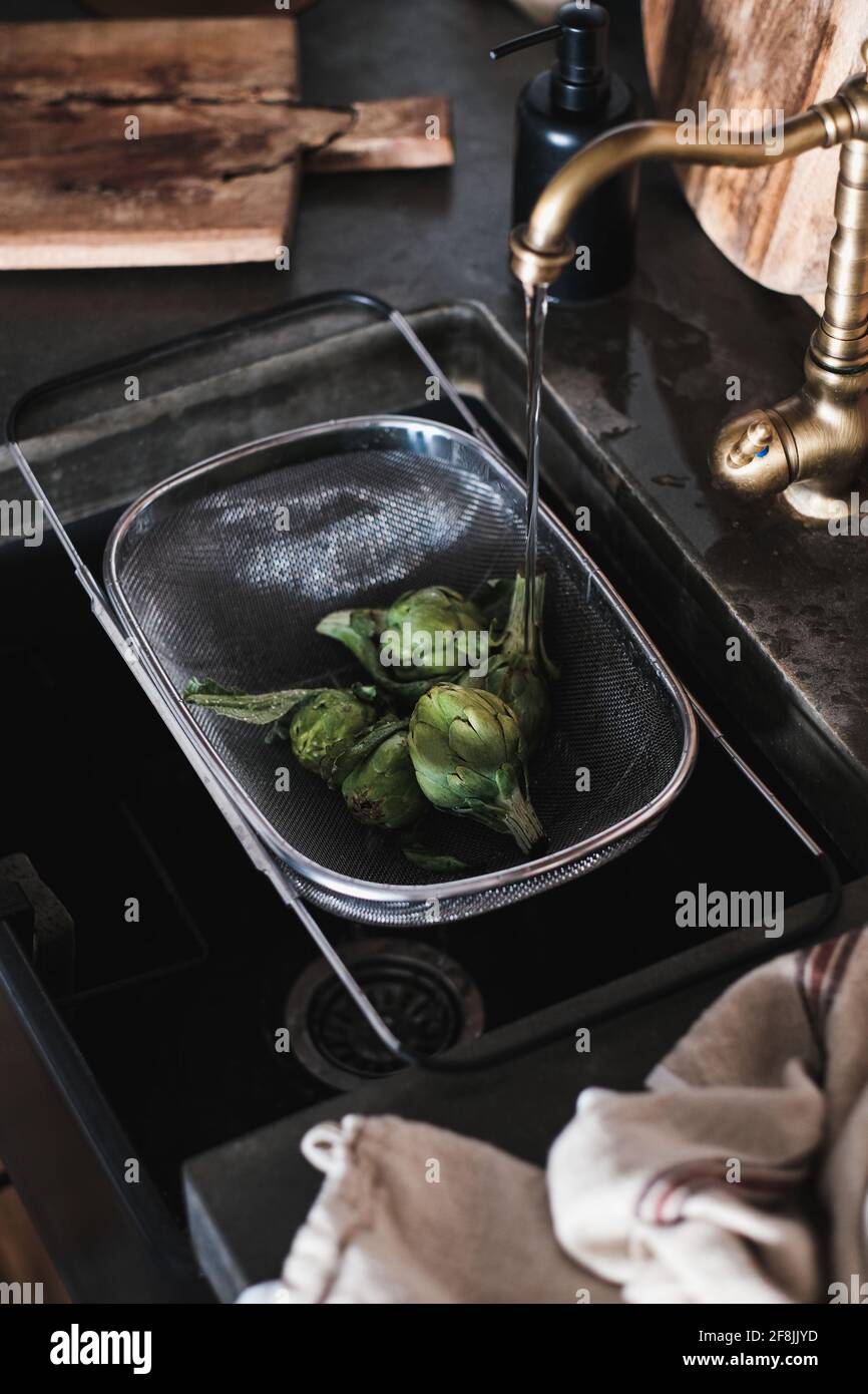 Frische grüne Baby Artischocken in Stahlsieb in der Küche sinc Stockfoto
