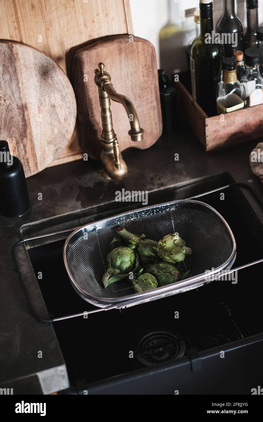Frische grüne Baby Artischocken im Sieb im Küchenwaschbecken, Draufsicht Stockfoto