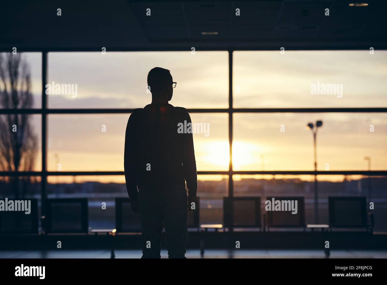 Nachdenklicher Passagier, der auf das Flugzeug wartet. Silhouette eines Mannes am Flughafen bei Sonnenaufgang. Stockfoto
