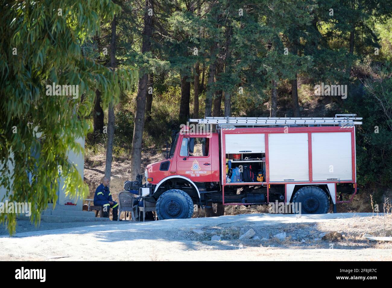 Eine griechische Feuerwehrmannschaft, die neben ihrem Feuerwehrmotor ruht. Die Besatzung ist als erste Reaktion auf Waldbrände in der Nähe eines Hügelwaldes stationiert. Stockfoto