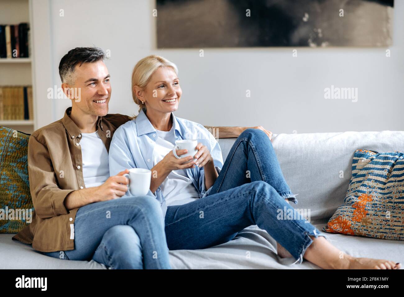Liebevoller glücklicher Erwachsener verheiratetes kaukasisches Paar in  stilvoller Freizeitkleidung, glücklicher Ehemann und Ehefrau sitzen auf dem  bequemen Sofa im Wohnzimmer, halten Tassen Tee, plaudern, verbringen Zeit  zu Hause Stockfotografie - Alamy