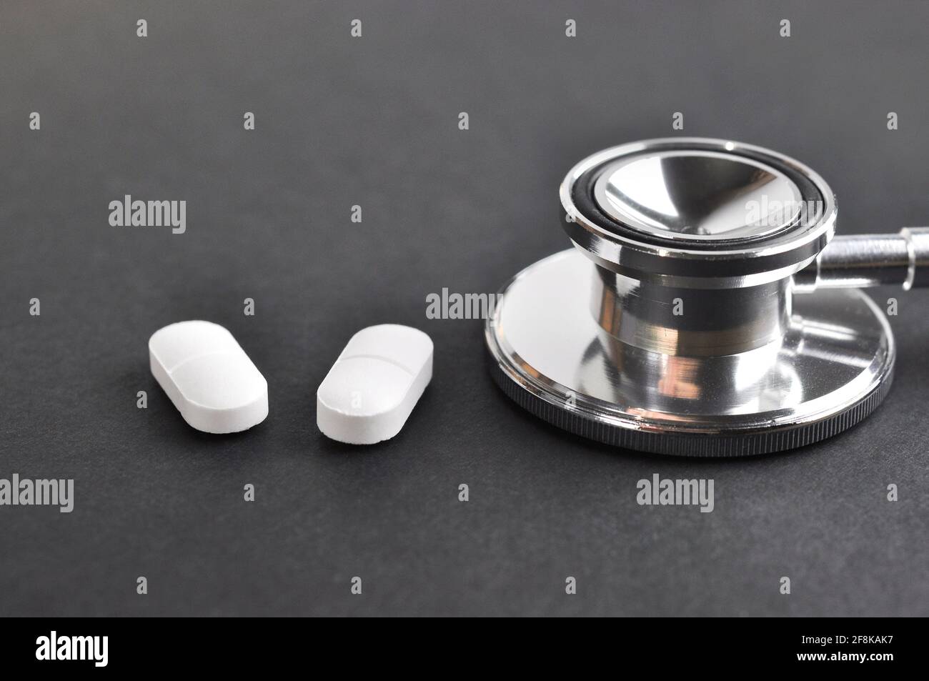 Stethoskop und Pillen auf schwarzer Oberfläche. Diagnose- und Behandlungskonzept. Stockfoto