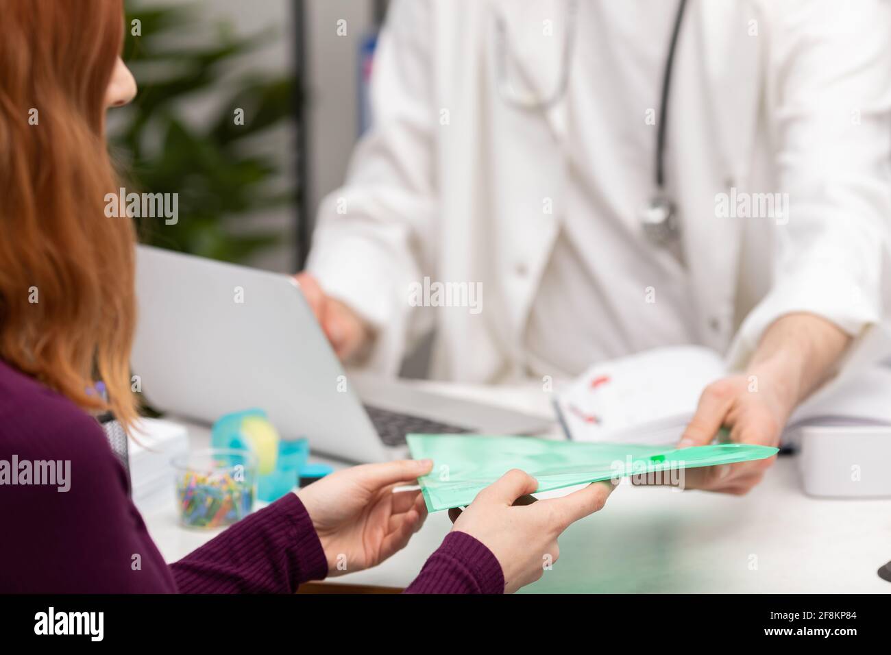 Eine Patientin mit roten Haaren übergibt ihrem Hausarzt Krankenakten. Arztpraxis. Nahaufnahme Stockfoto