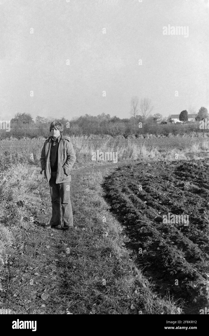 Junger männlicher Teenager in ausgestellter Jeans und Parka im Stehen Ein ländliches Feld Mitte der 1970er jahre england großbritannien Stockfoto