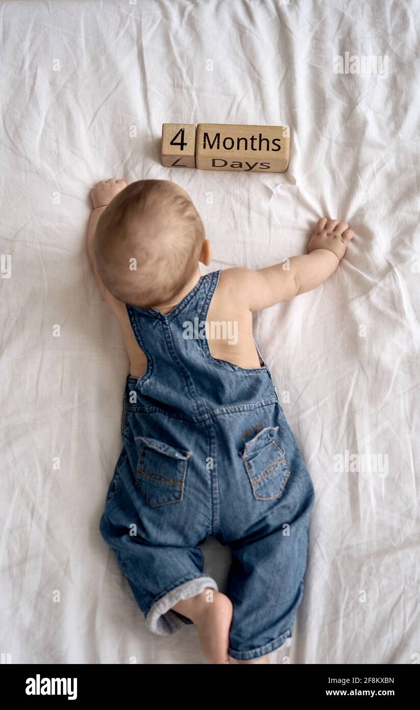 Entzückende vier Monate alten Baby Junge in Denim Latzhose liegen Auf weißem Bett Stockfoto