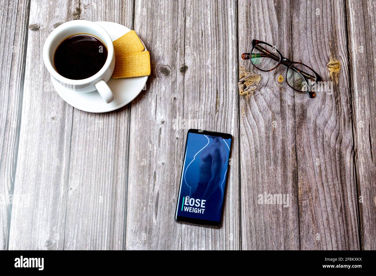 Ein Mobiltelefon oder Mobiltelefon, das auf einem Holzboden liegt Tabelle mit der App „Männer verlieren Gewicht“ auf dem Bildschirm Stockfoto