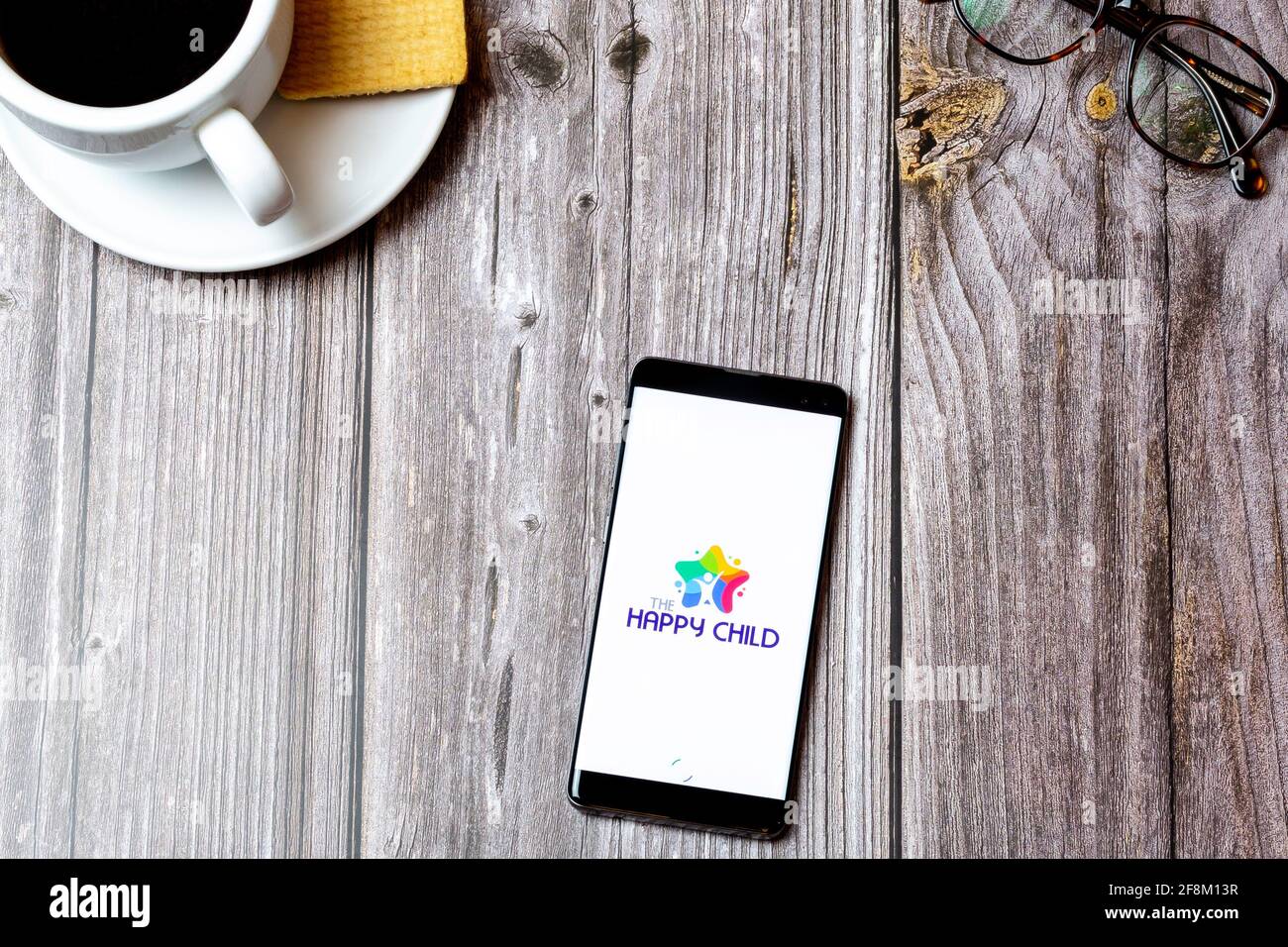 Ein Mobiltelefon oder Mobiltelefon, das auf einem Holzboden liegt Tabelle mit der Happy Child-App auf dem Bildschirm Stockfoto