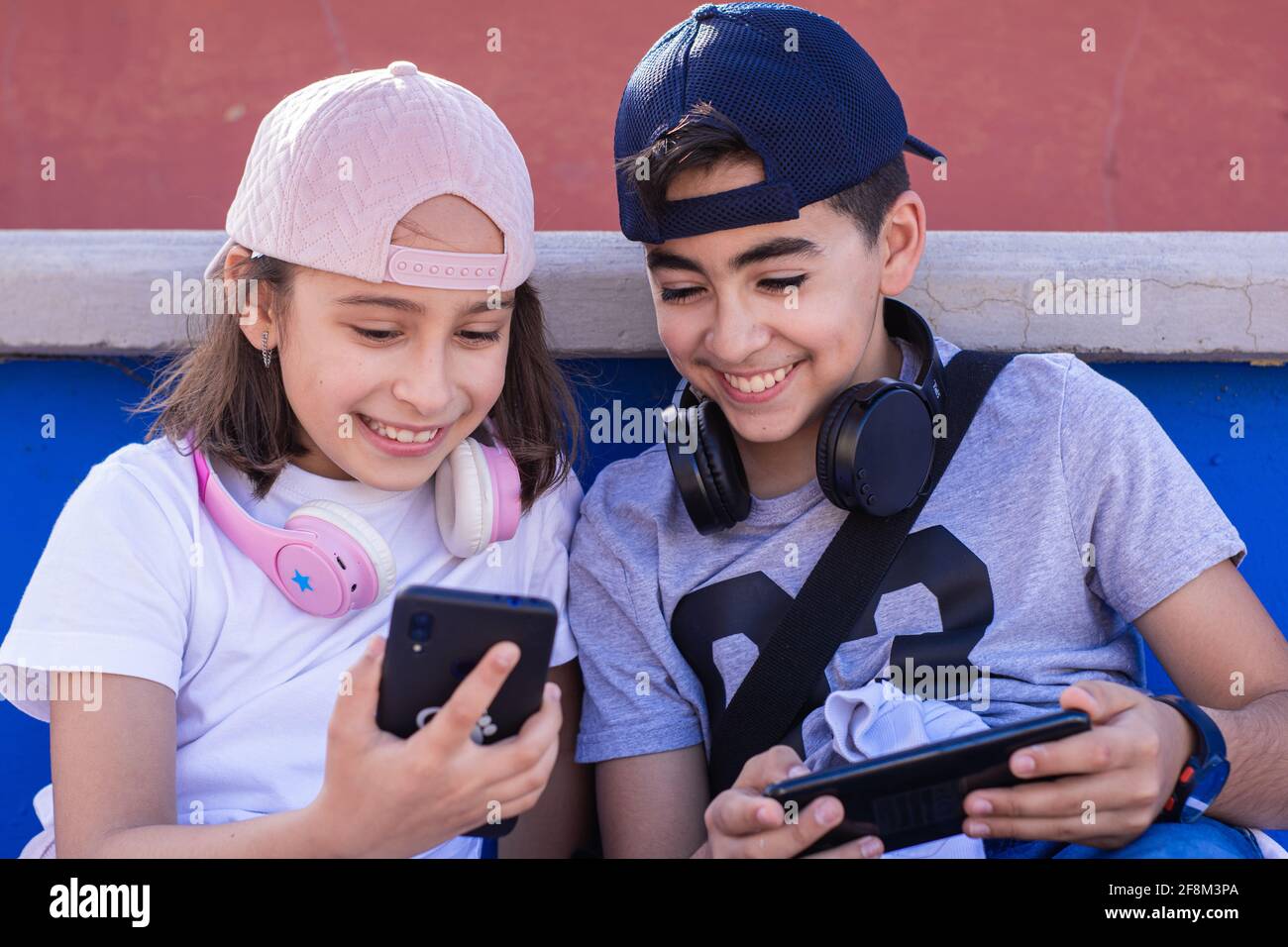 Zwei kaukasische Jugendliche, sehr lächelnd, mit mobilen Geräten und Kopfhörern, zeigen sich ihre Handys auf der Tribüne. Stockfoto