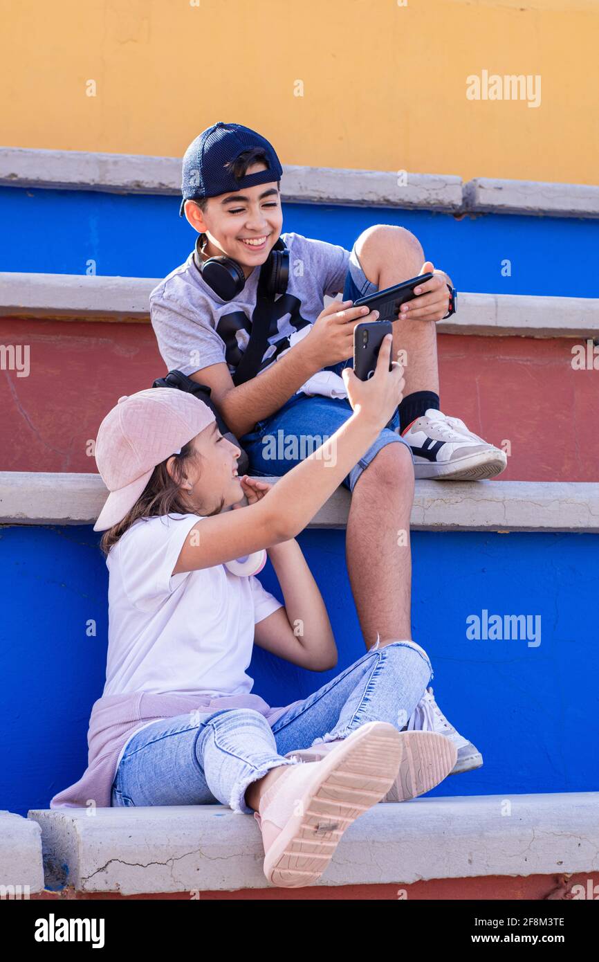 Zwei kaukasische Jugendliche, sehr lächelnd, mit mobilen Geräten und Kopfhörern, zeigen sich ihre Handys auf der Tribüne. Stockfoto