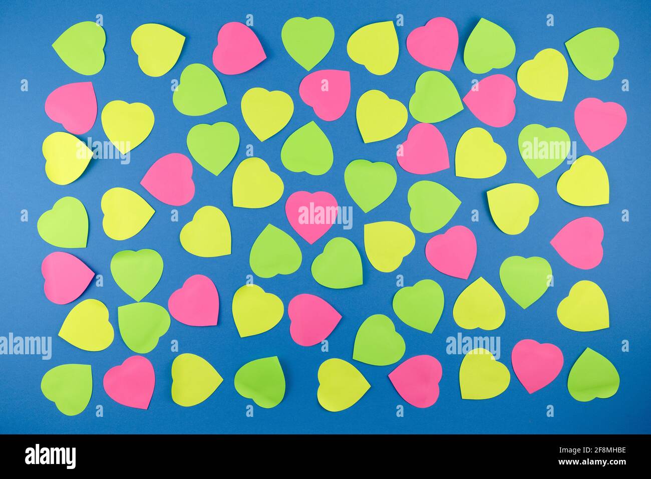 Neon-Haftnotizen in Herzform auf blauem Hintergrund. Liebe am Valentinstag Datum Idee Kunst Konzept Stockfoto