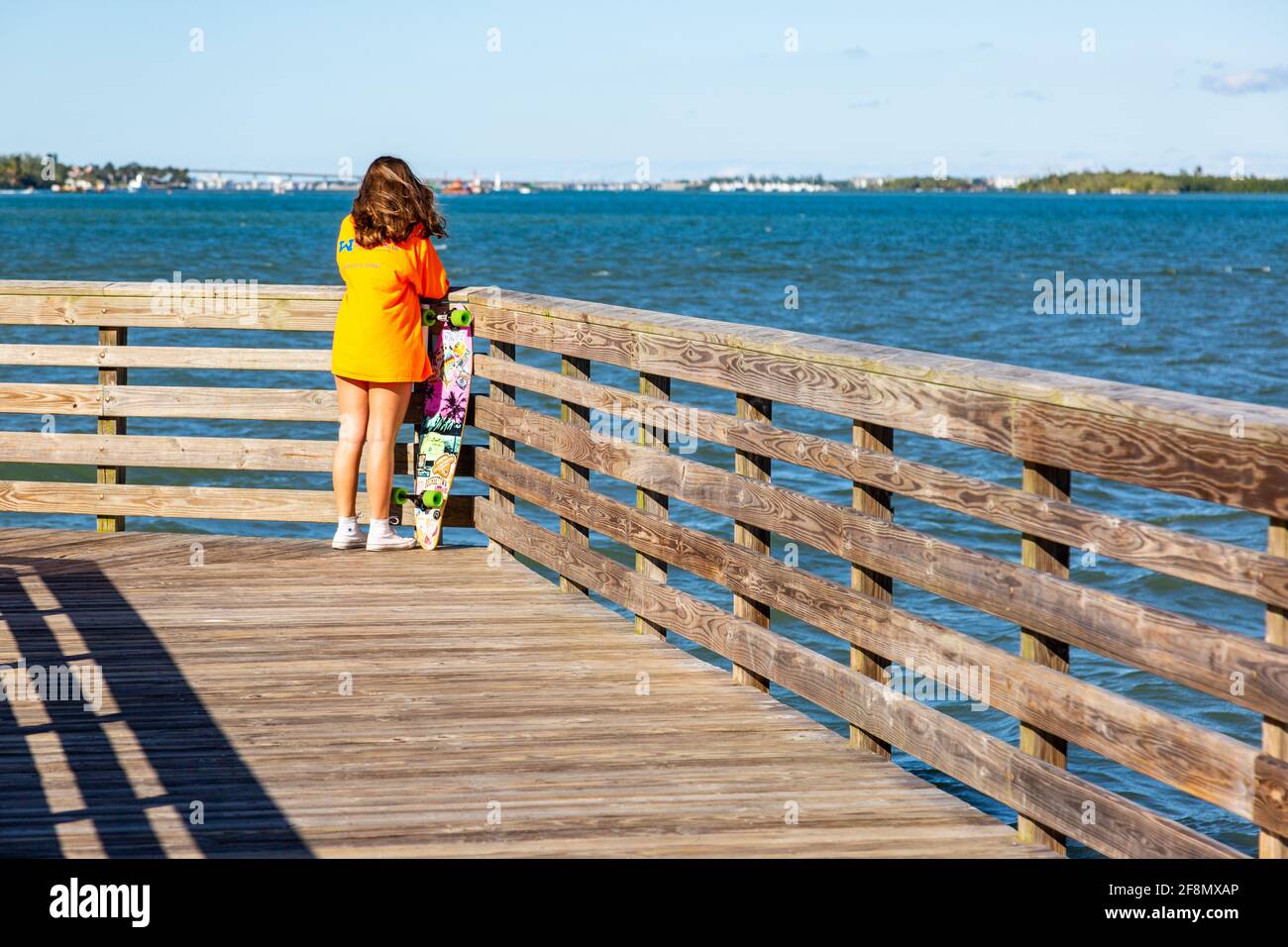Ein junges Mädchen steht mit ihrem Longboard und blickt auf den Zusammenfluss des St. Lucie River und der Manatee Pocket im Twin Rivers Park, Port Salerno, Florida Stockfoto