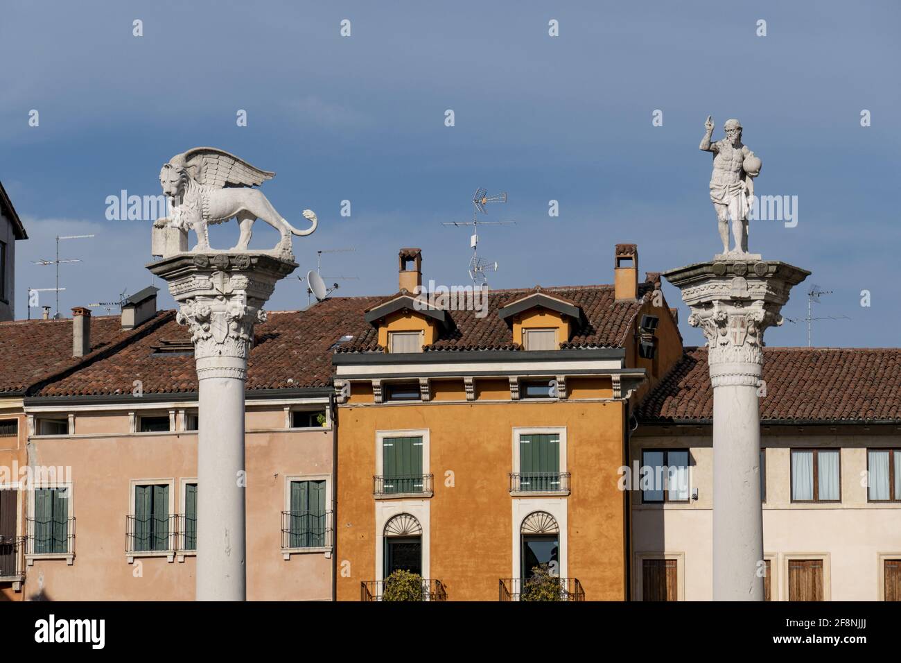 Statue eines geflügelten Löwen und eines Männchens auf dem Säulenoberseite im Hintergrund von Gebäuden in Italien Stockfoto