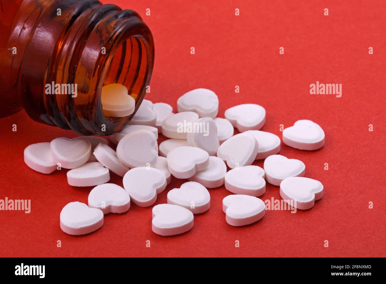 Herzförmige Pillen aus Flaschenglas auf rotem Hintergrund Medikamente, die Menschen helfen Stockfoto