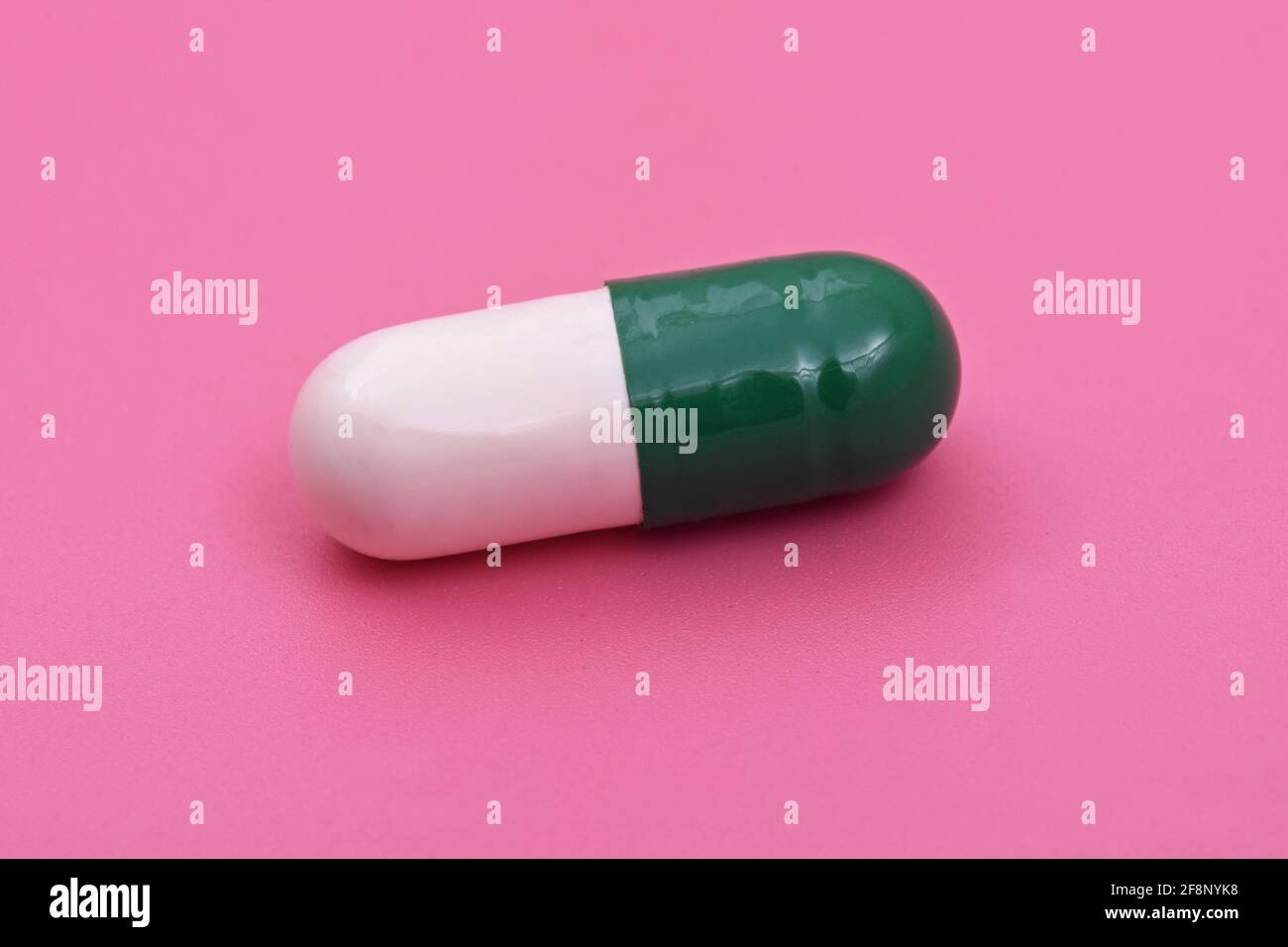 Weiße grüne Kapsel Pharmazeutische Medizin Tablette auf rosa Hintergrund, flache Lay Copy Raum Medizin Konzepte Baby rosa Farbe Hintergrund Stockfoto
