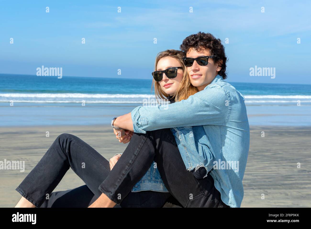 Junges Paar in Sonnenbrillen und am Strand sitzen Stockfoto