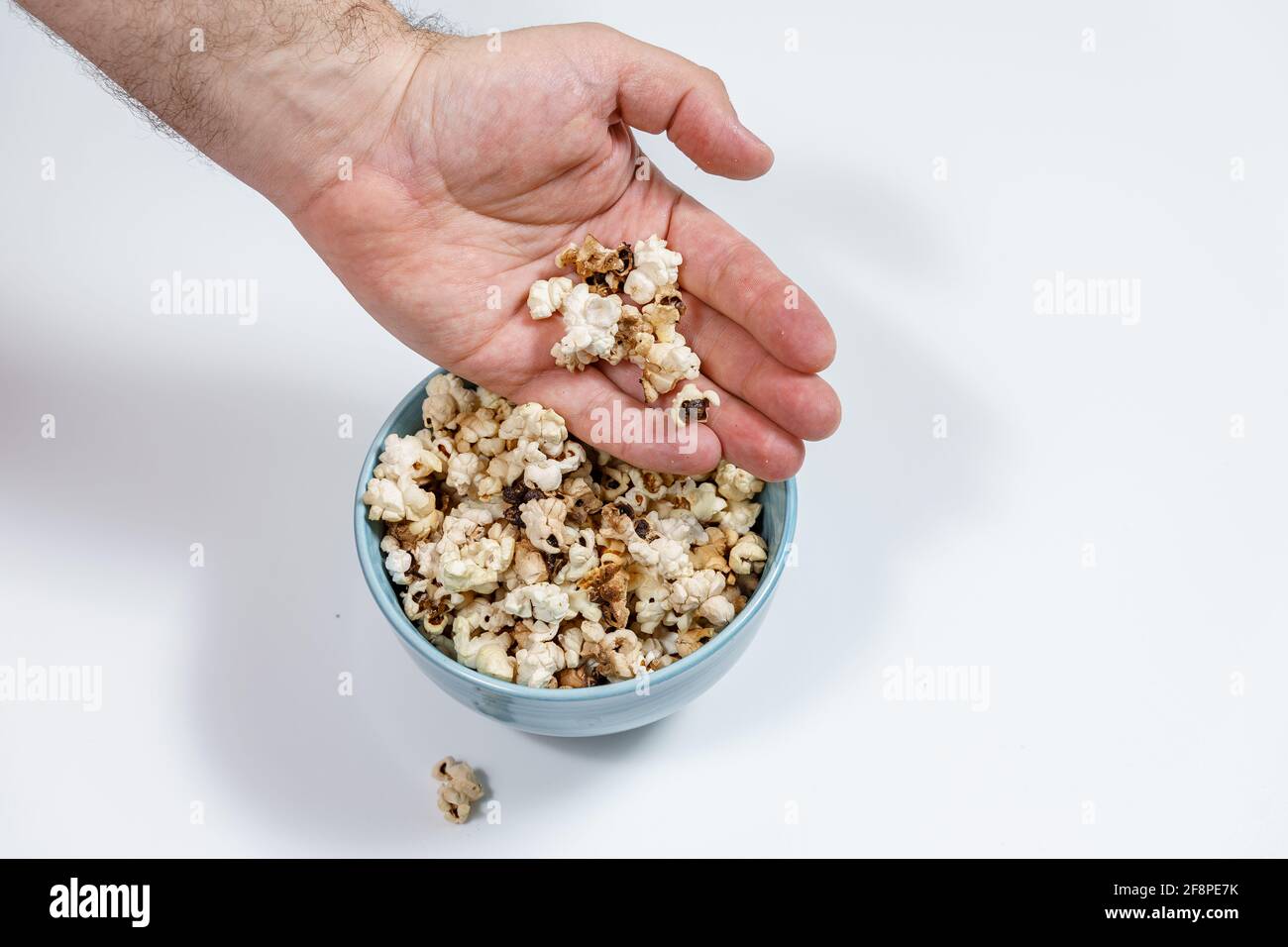 Verdorbenes verbranntes Popcorn in einer blauen Tasse. Hand des Mannes aus der Nähe Stockfoto