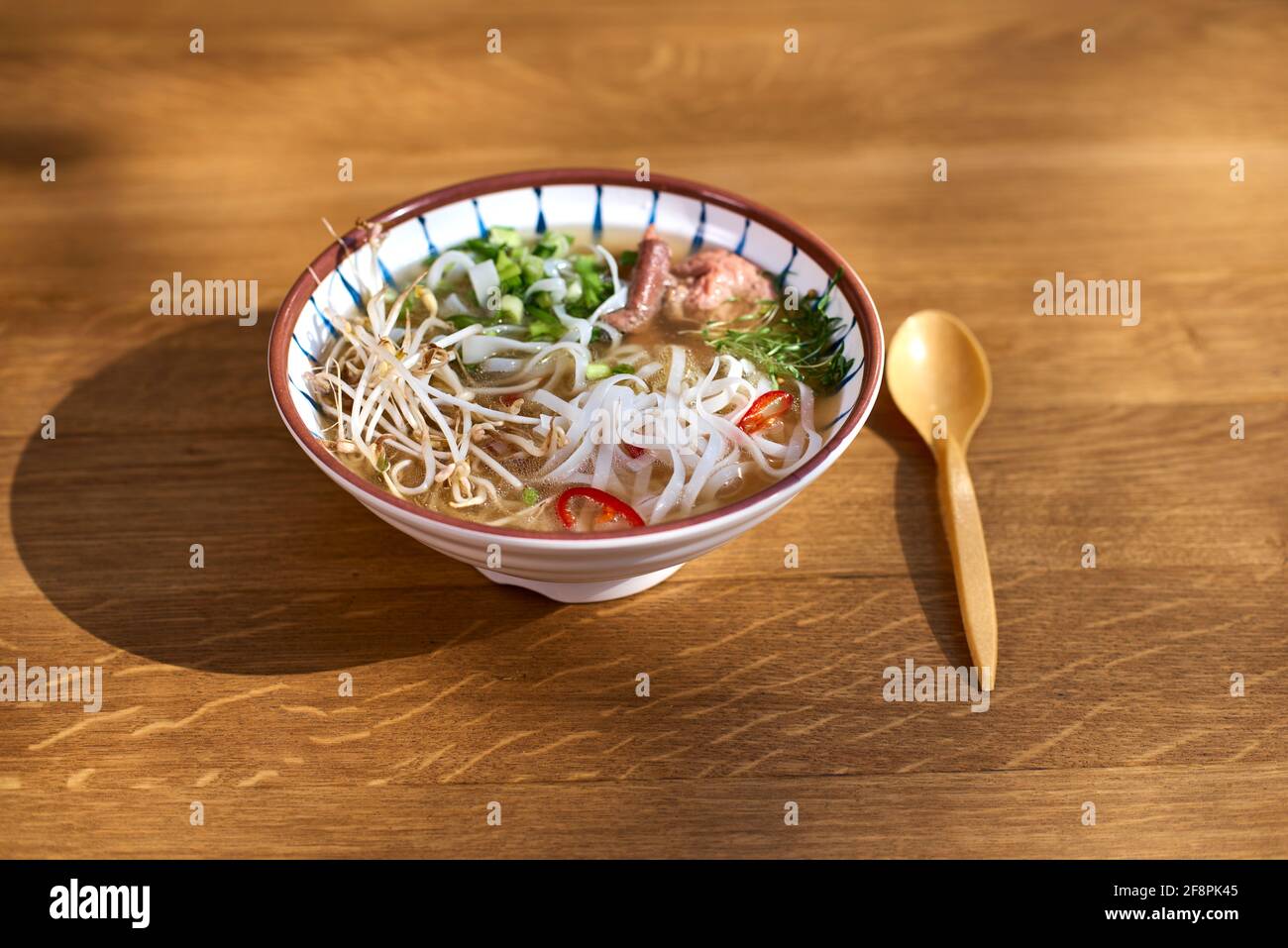 Asiatische Pho bo-Suppe, beste Pho-Brühe, in einer leichten Schüssel auf einem Holztisch. Kopierbereich, selektiver Fokus Stockfoto
