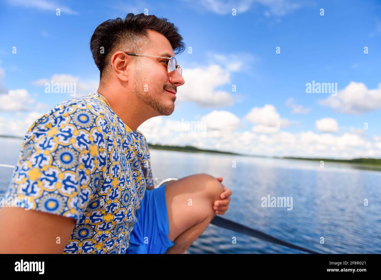 Junger Mann sitzt auf einem Hauptdeck eines Segelbootes und segelt auf einem See. Sommerferien, Kreuzfahrt, Erholung, Sport, Regatta, Freizeitaktivitäten, Service, To Stockfoto
