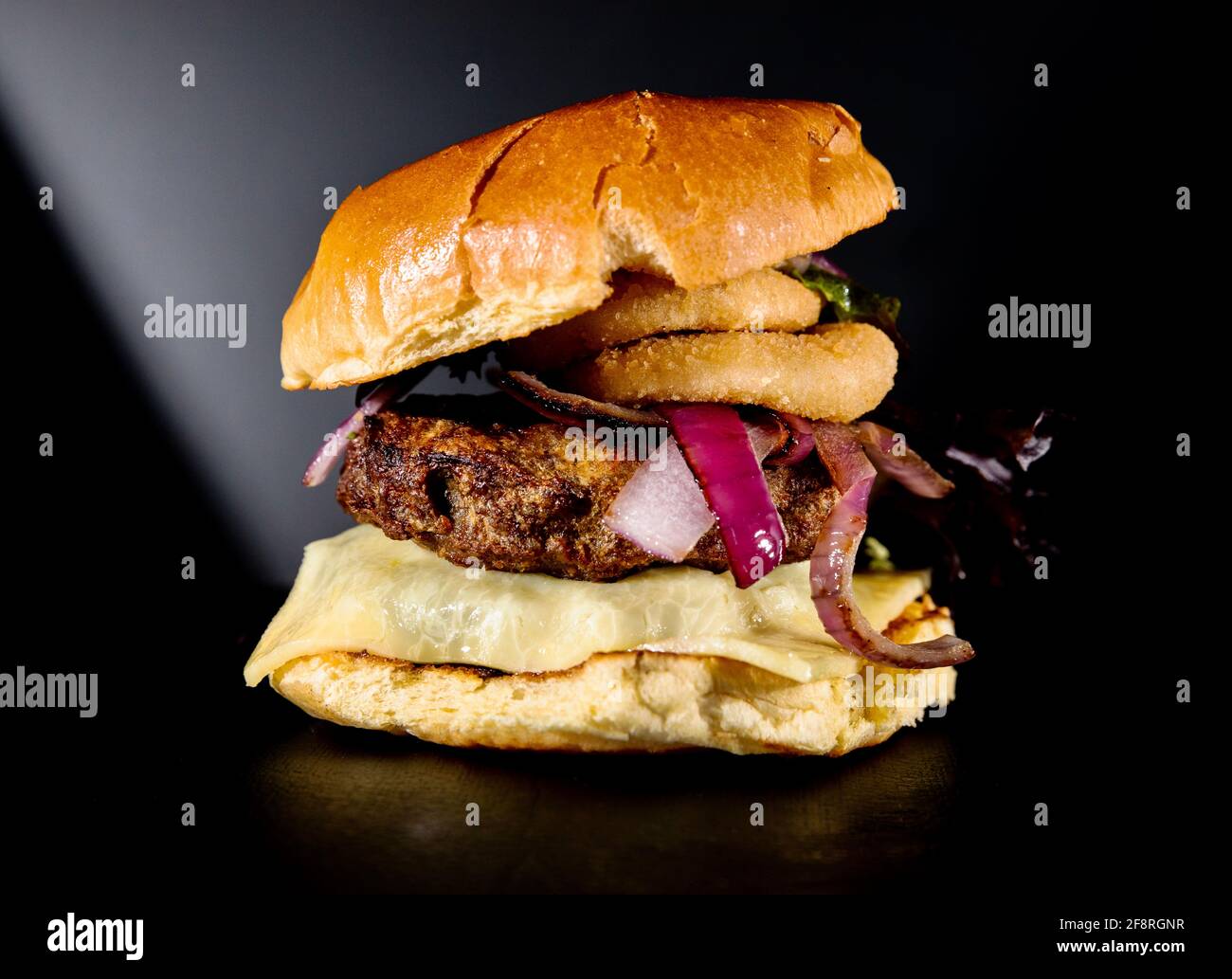 Ein Burger mit Zwiebel klingelt vor dunklem Hintergrund Stockfoto